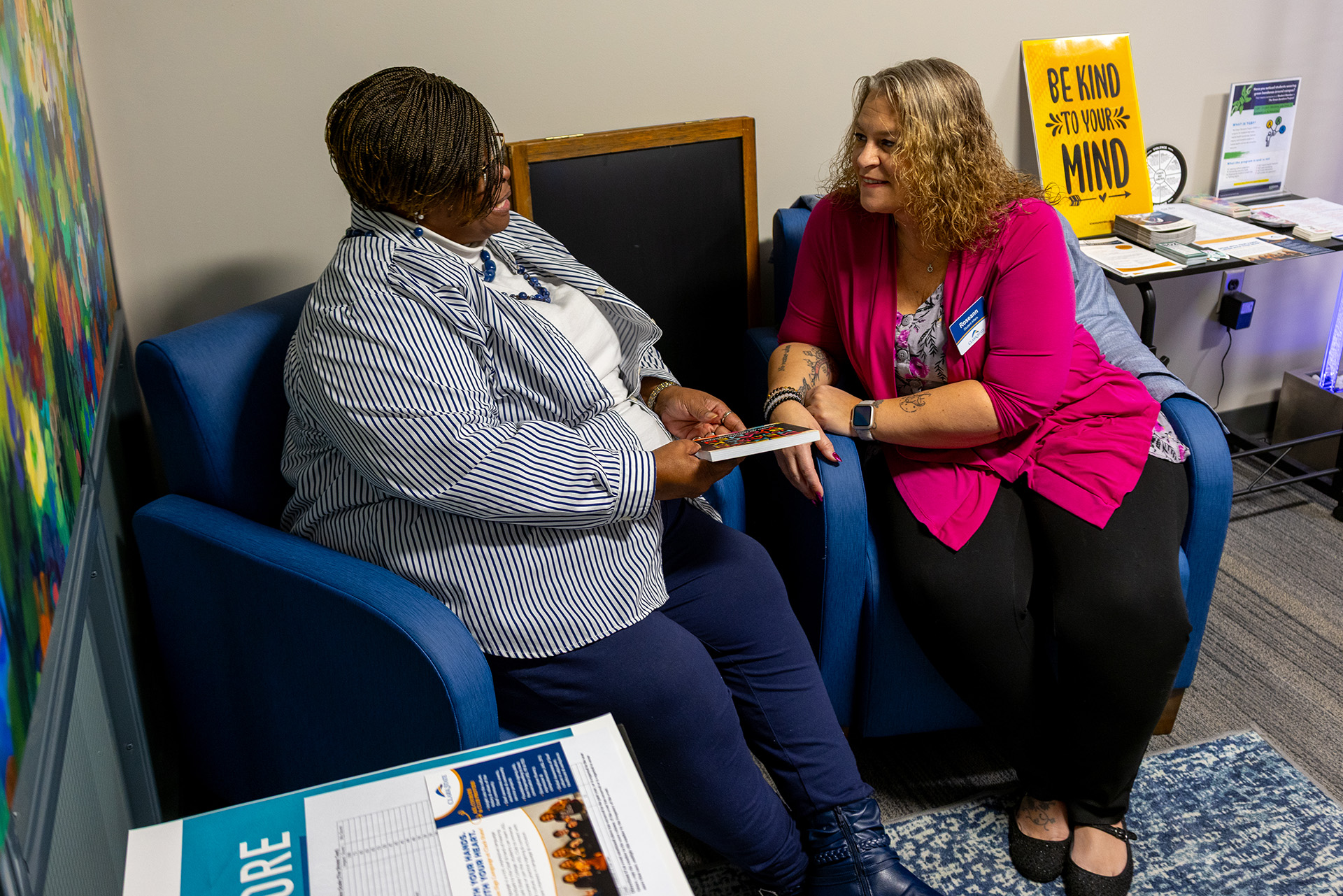 Two women sitting in navy chairs discussing a book.