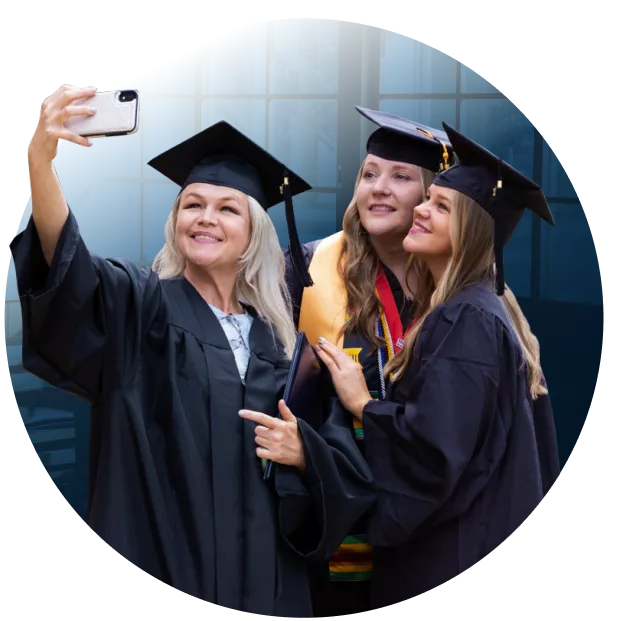 3 Female Graduates in caps and gowns taking selfie